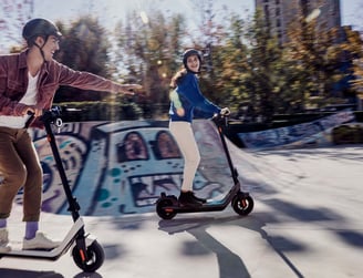a man and woman riding scooters in a skateboard park