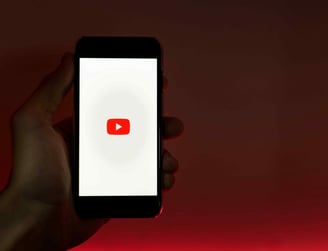 Hand holding a phone displaying the YouTube logo on a dark background
