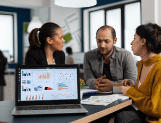 Team discussing data insights with graphs and charts displayed on a laptop.