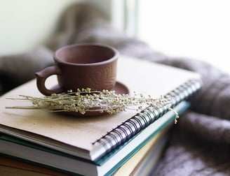 A photo of a purple mug sitting on a stack of brown books.