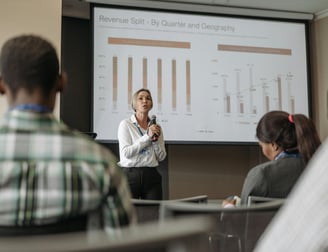 Mulher palestrando em evento, apresentando slides com equipamentos funcionando perfeitamente.