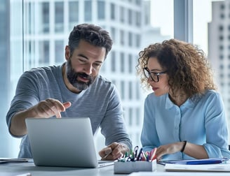 Two people sitting in office looking at a laptop.