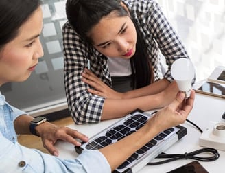 Deux femmes discutant d'une ampoule LED avec un clavier en braille sur la table.