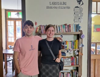 One student and one teacher standing in front of a bookshelf with a quote about travel and reading o