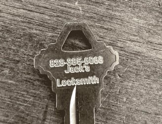 Metal key engraved with "Jack's Locksmith" and phone number, representing professional locksmith services.