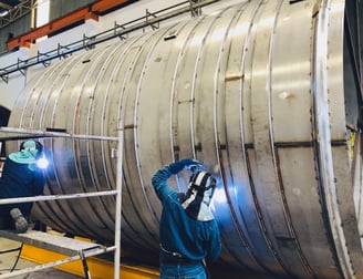 a man welding a large metal pipe in a factory
