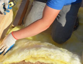 Artisan installant de la laine de verre pour isoler une toiture, garantissant un meilleur confort thermique dans une maison d
