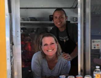 a woman and man are standing in front of a food truck