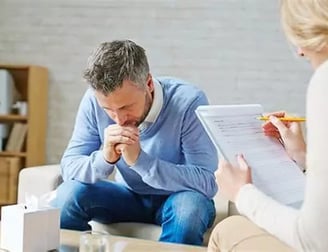 Femme aidante écoute un homme penché en avant coudes sur ses cuisses