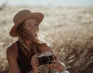 Portrait of a woman in a hat, she is holding a camera and smiling