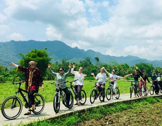Wisatawan bersepeda santai menyusuri jalan pedesaan dengan pemandangan sawah dan Candi Borobudur di kejauhan