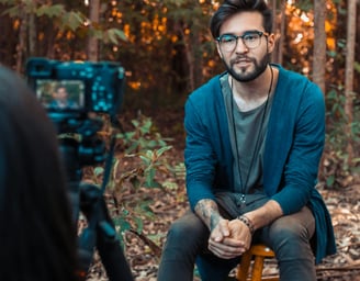 Man being interviewed on camera while sitting in forest 