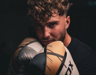 Barbat cu manusi de box RDX, in garda, priveste concentrat spre camera.