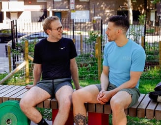 A personal trainer in a blue t-shirt sat outside talking to his client