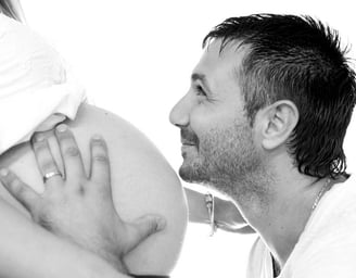 Photo de grossesse en noir et blanc, portrait du futur papa embrassant le ventre