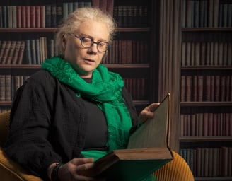 Femme sénior lisant un vieux livre dans fauteuil jaune, fond bibliothèque