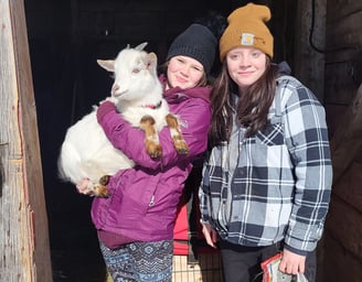 two young girls standing together one of them is holding a white goat