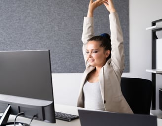 a woman sitting at a desk with her arms up in the air stretching
