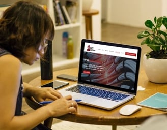 a woman sitting at a table with a laptop and a cell phone