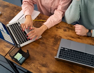 a woman sitting at a desk with a laptop and a man