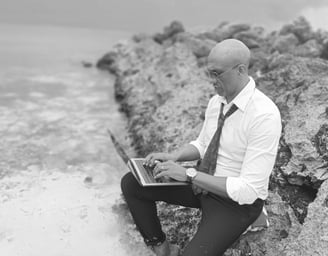 « Bruno Valery travaillant sur son ordinateur, assis sur un rocher les pieds dans l’eau en Guadeloupe »