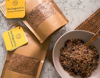Chocolate Panjeeri/ granola served in a bowl alongside sealed, recyclable brown paper bags
