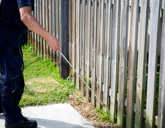 A man is spraying pesticide outdoors near a wooden fence. 