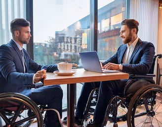 Zwei Rollstuhlfahrer sitzen für ein Beratungsgespräch in einem Café