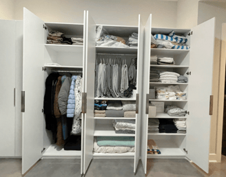 Neatly organized white wardrobe with folded linens, baby items, and hanging coats.