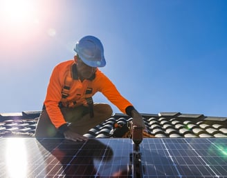 um instalador no telhado fixando um módulo fotovoltaico com uma parafusadeira