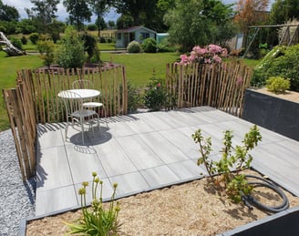 Petite terrasse carrelée avec mobilier de jardin, bordée d'une palissade en bois naturel