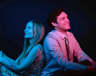a man in red light and woman in blue light sitting back to back looking at opposite direction