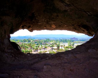 a hole in a rock formation showing a city with mountains behind