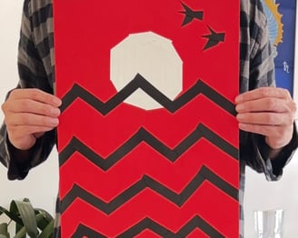 papel vermelho, onde um sol branco está desenhado com fitas, que também fazem o desenho de ondas pretas e duas aves no céu.