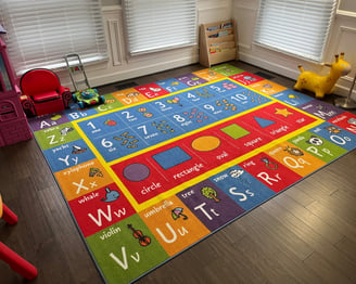 Photo of daycare room where children play. Large colorful floor mat and bookshelf.