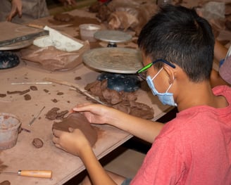 Young boy wearing a mask playing with clay at a table.