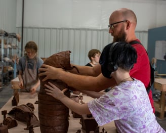 A teacher and middle school student holding a big clay creature up.