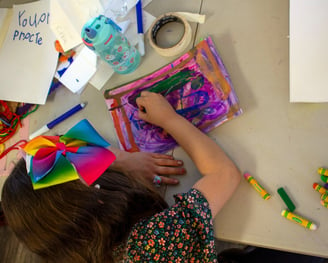 Young child using pastels to create a colorful piece of art on paper.