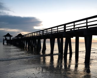 shadowy sunset view of naples pier in naples florida, with waves and the ocean and clouds 