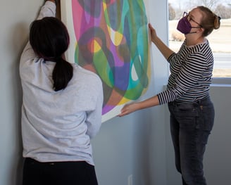 Two individuals hanging a colorful painting on one of our walls.