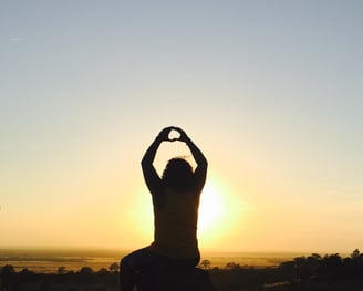 Man sitting down watching the sunset with his hands in the air