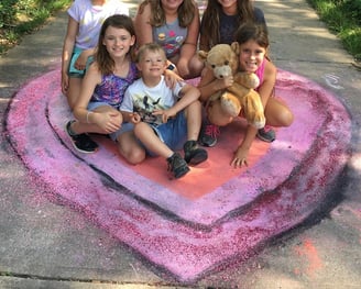 Group of smiling children posing on top of a large chalk heart they made.