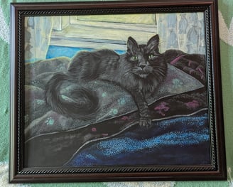 Cherry oak framed arcrylic portrait painting of a long haired black cat with very green eyes laying in his blanketed bean bag