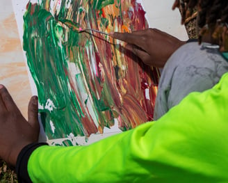 Young boy using a palette knife to smooth paint dabs over a paper.