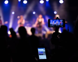 a person holding a cell phone in front of a stage with a video camera live streaming on facebook