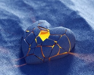 Un cœur avec des émaux bleus et une lumière dorée à l'intérieur posé sur du sable bleu, amour