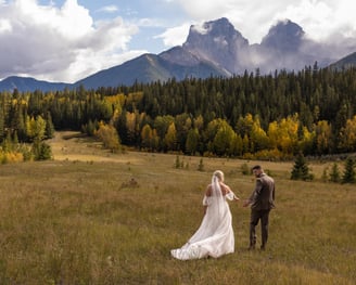 a bride and groom walking through a field in Canmore