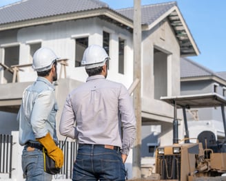 two men in hard hats standing in front of a house