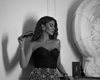 A glamorous brunette woman wearing jewelry in black lace top and sequins skirt holding black sunglasses looking to the right