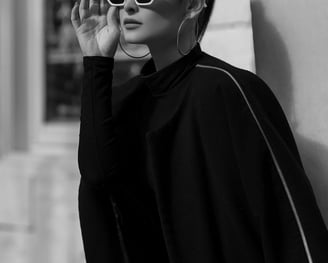 A stylish brunette woman with hoop earrings in all black wearing holding her white sunglasses with her right hand